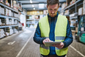 A logistics manager in a warehouse taking notes